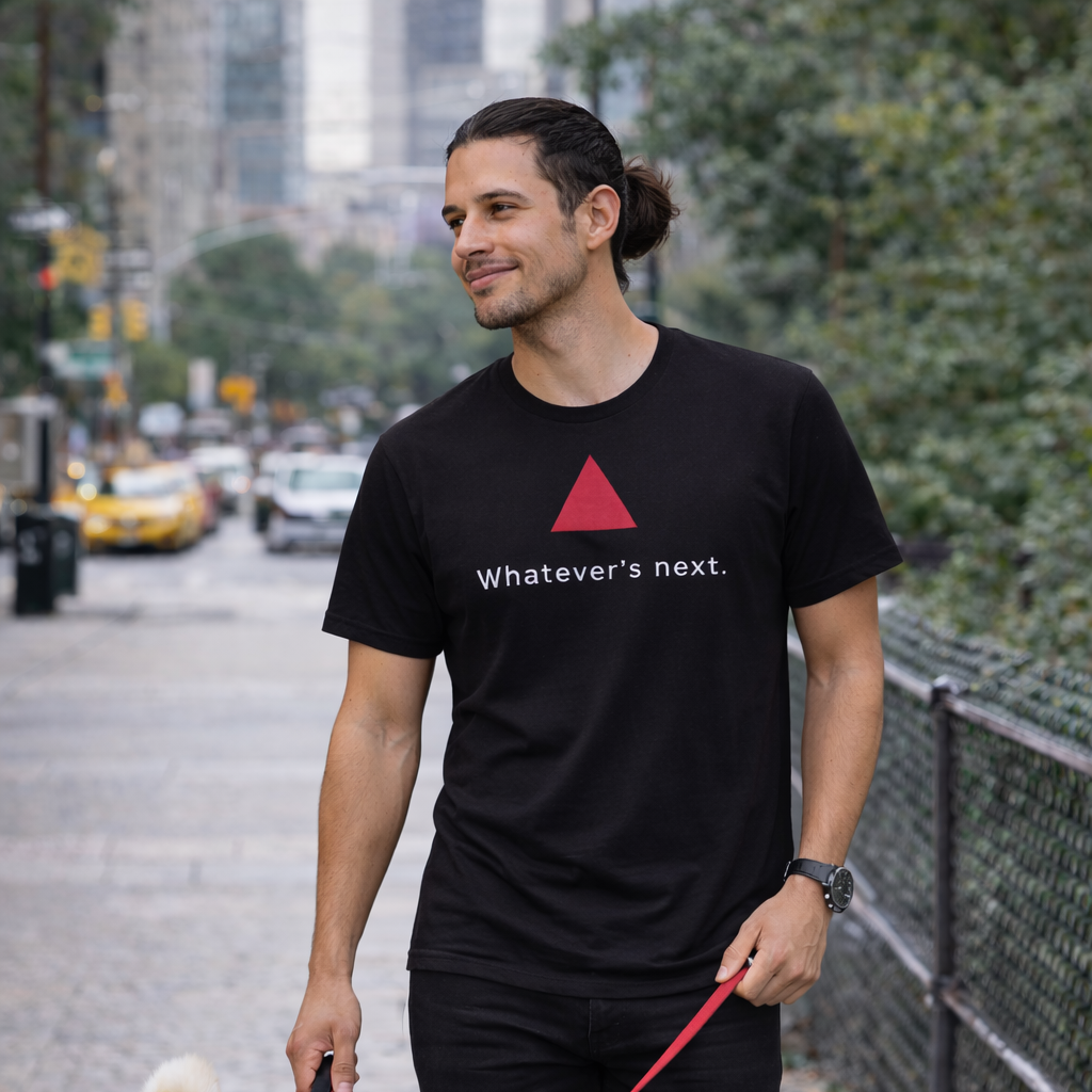Model wearing a black t-shirt with a red triangle and text, walking in front of a city skyline.